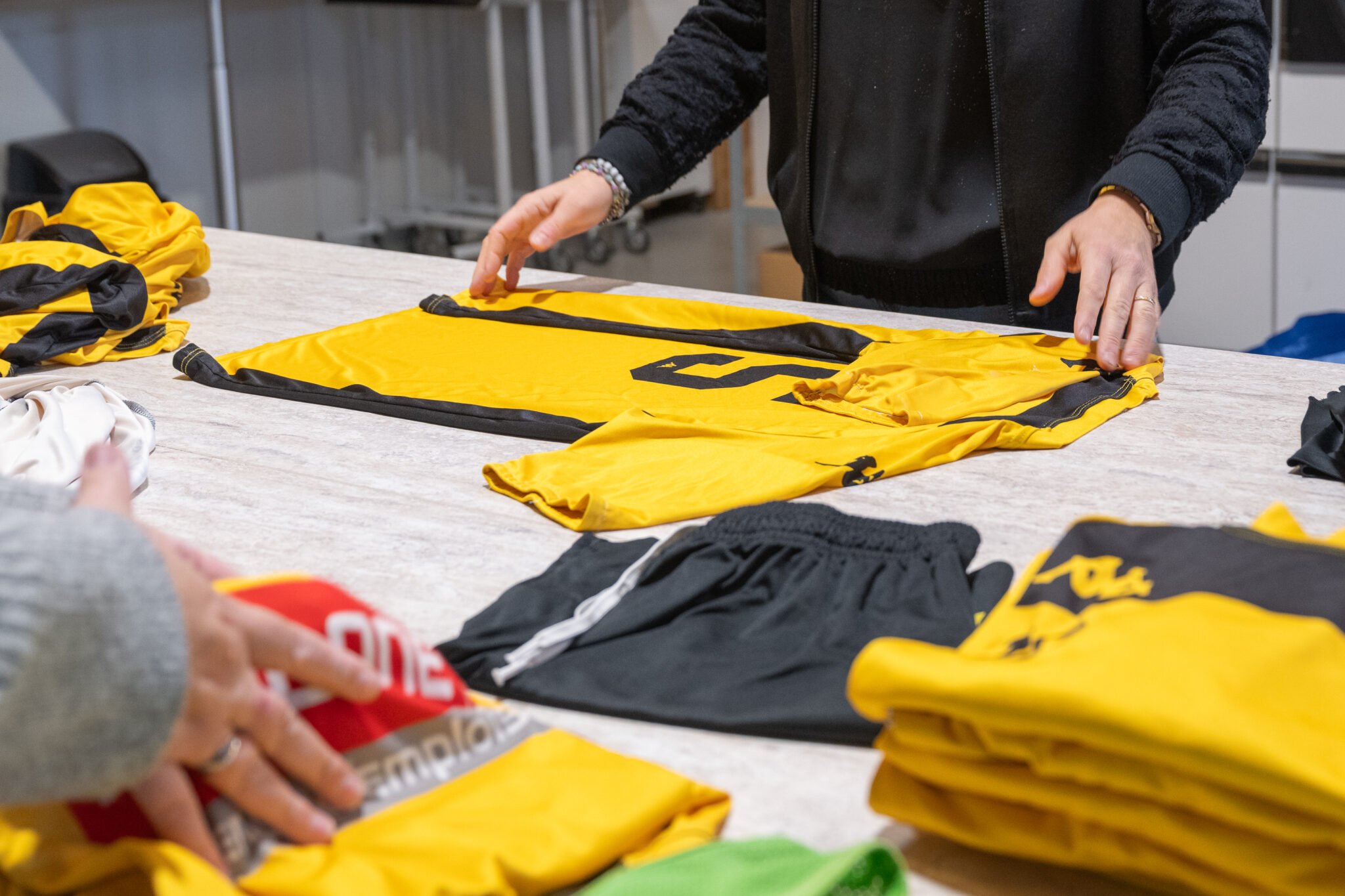 Personnes pliant des maillots de sport jaunes sur table.
